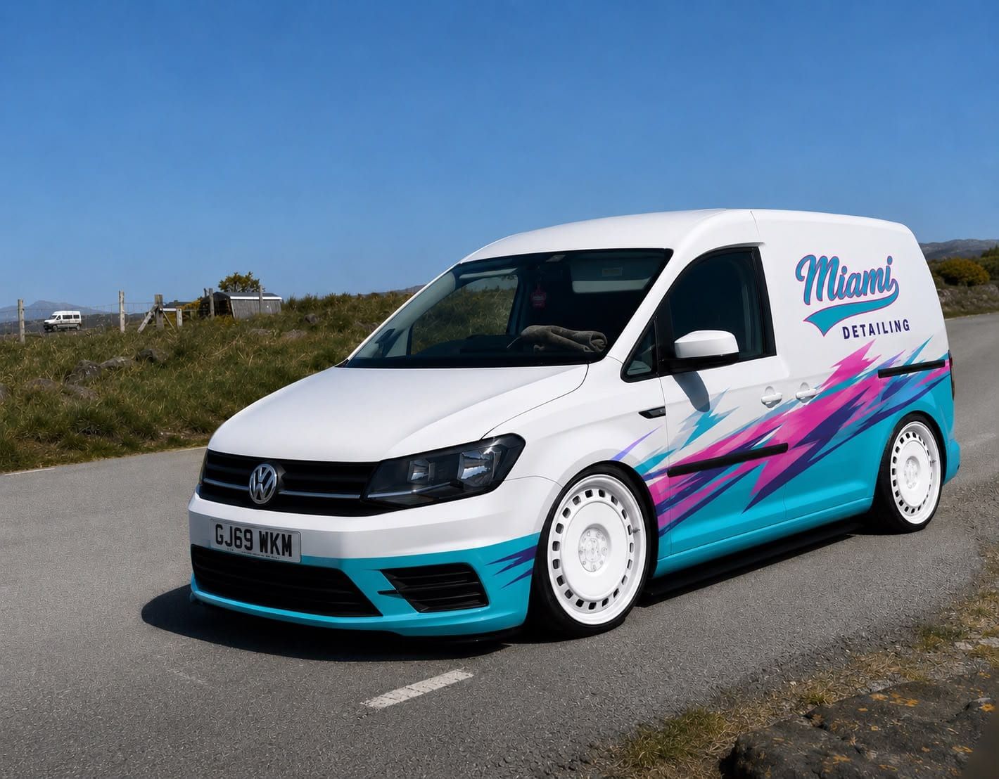 White VW Caddy van with a teal and pink graphic wrap reading "Miami Detailing", parked on a country road.
